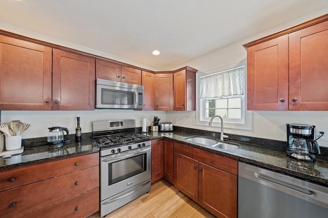 kitchen featuring stainless steel appliances, recessed lighting, light wood-style floors, a sink, and dark stone countertops