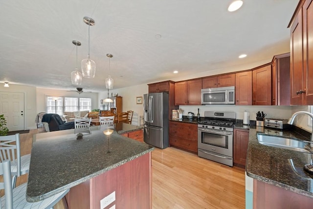 kitchen with dark stone countertops, appliances with stainless steel finishes, light wood-type flooring, and a sink