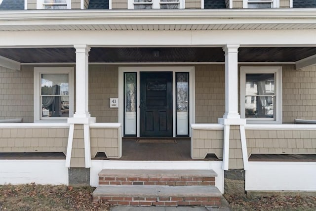 entrance to property with covered porch and roof with shingles