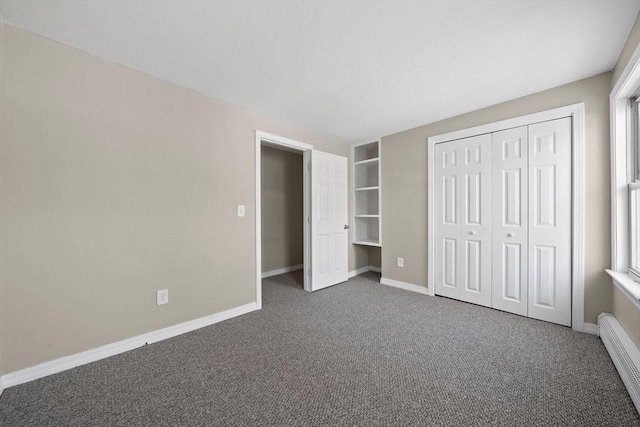 unfurnished bedroom with baseboard heating, dark carpet, and a closet