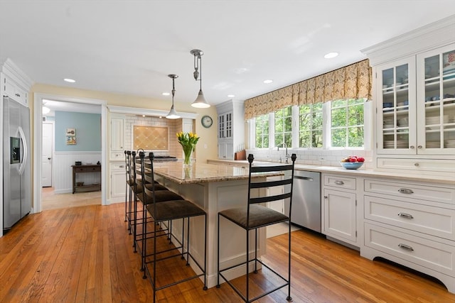 63 Claypit Hill Rd, Wayland, MA 01778 - kitchen with appliances with stainless steel finishes, a kitchen breakfast bar, a kitchen island, glass insert cabinets, and light wood-style floors
