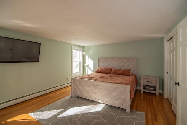 bedroom featuring a baseboard heating unit, hardwood / wood-style floors, and a closet