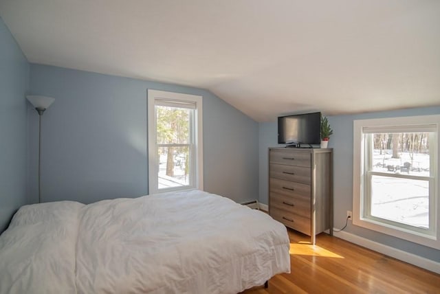 bedroom with a baseboard radiator, lofted ceiling, and light hardwood / wood-style flooring