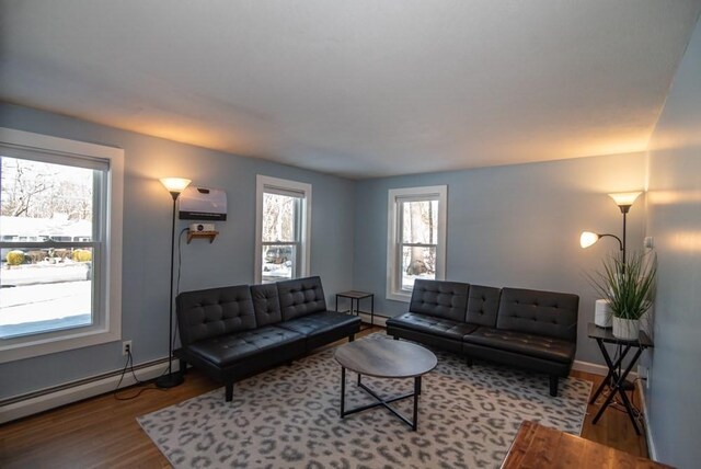 living room with a baseboard heating unit, a wall mounted air conditioner, and wood-type flooring