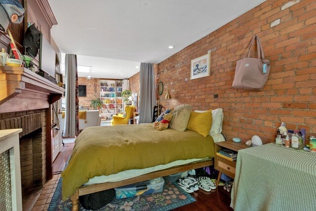 bedroom featuring wood finished floors, brick wall, and a fireplace