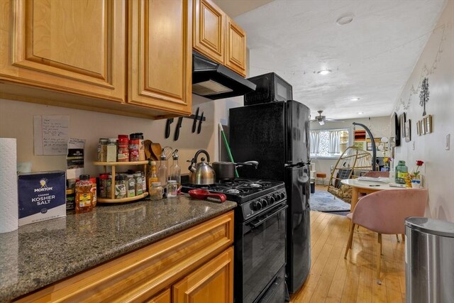 kitchen with light wood-style floors, dark stone countertops, recessed lighting, under cabinet range hood, and black appliances