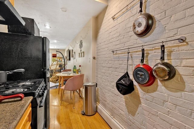 kitchen featuring brick wall, black appliances, and light wood-type flooring