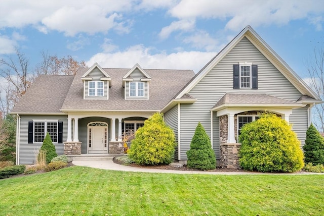 cape cod-style house with a shingled roof, a front yard, stone siding, and covered porch