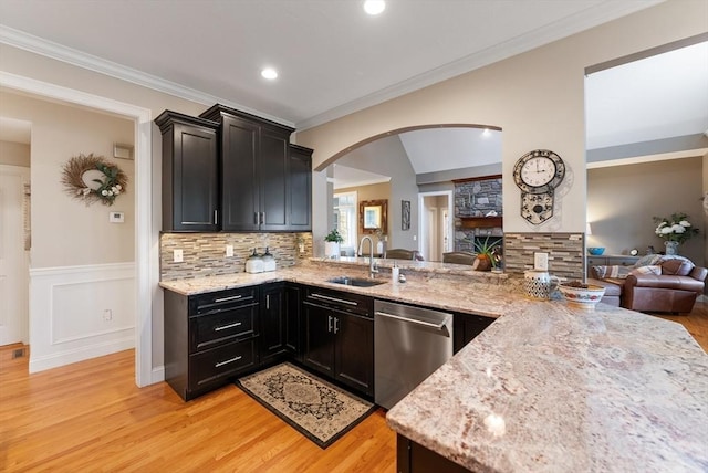 kitchen featuring arched walkways, dishwasher, a sink, light stone counters, and light wood finished floors