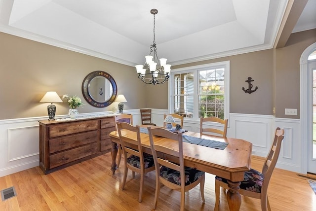 dining space with visible vents, a decorative wall, light wood-style floors, a raised ceiling, and a wainscoted wall