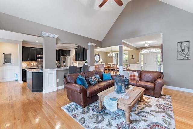 living area with arched walkways, high vaulted ceiling, ceiling fan with notable chandelier, light wood-style floors, and ornate columns