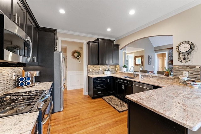 kitchen with arched walkways, a sink, dark cabinets, ornamental molding, and stainless steel appliances