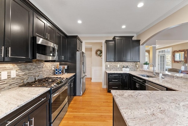 kitchen with ornamental molding, a sink, dark cabinetry, arched walkways, and appliances with stainless steel finishes