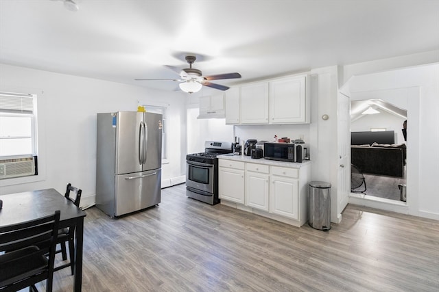 kitchen with light wood-type flooring, appliances with stainless steel finishes, white cabinetry, and ceiling fan