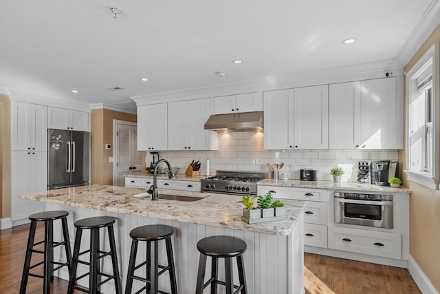 kitchen featuring high end appliances, white cabinetry, a sink, wood finished floors, and under cabinet range hood