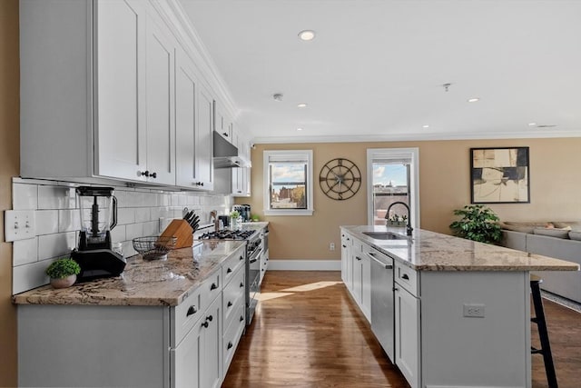 kitchen featuring a breakfast bar, crown molding, appliances with stainless steel finishes, a sink, and under cabinet range hood