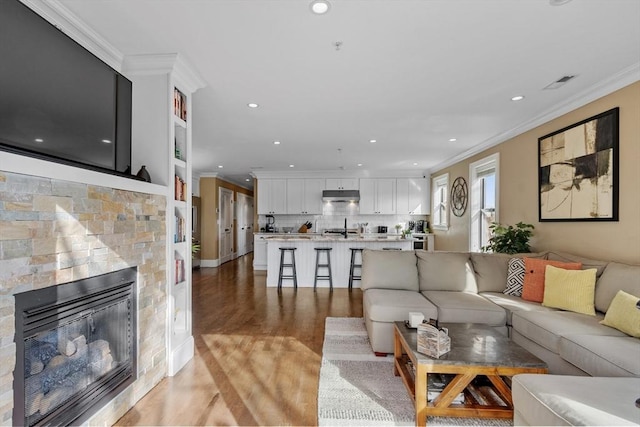 living area featuring visible vents, crown molding, light wood-type flooring, a fireplace, and recessed lighting