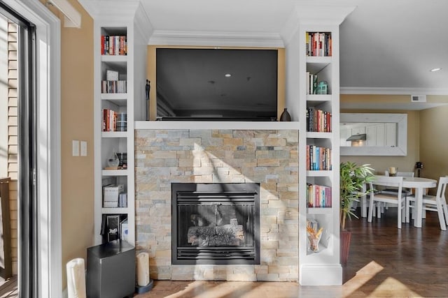 interior space featuring built in features, visible vents, ornamental molding, wood finished floors, and a fireplace