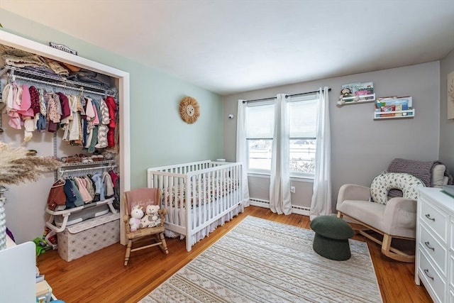 bedroom with a crib, a baseboard radiator, light wood-type flooring, and a closet