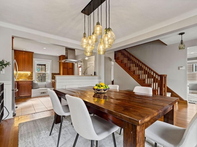 dining area featuring crown molding, stairway, and light wood-style flooring