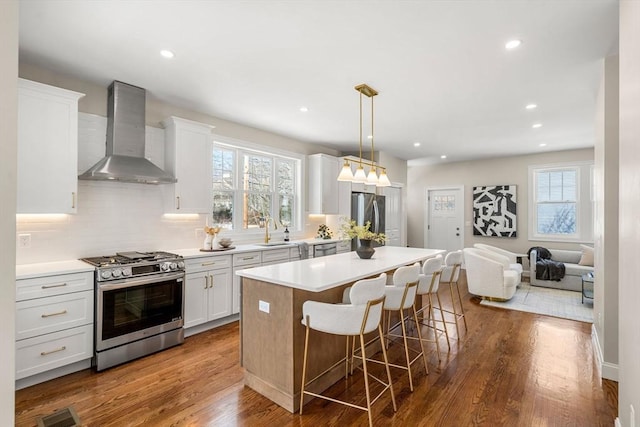 kitchen with white cabinetry, a center island, hanging light fixtures, stainless steel appliances, and wall chimney range hood