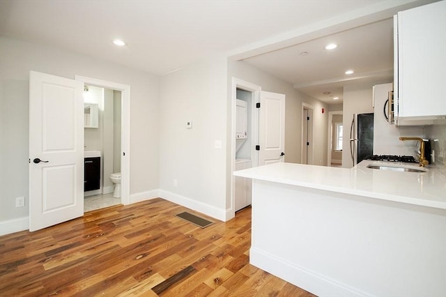 89 Morris St, Boston, MA 02128 - kitchen with stainless steel appliances, recessed lighting, white cabinetry, light wood-style flooring, and stacked washer / dryer