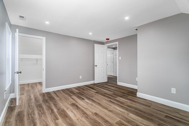 unfurnished bedroom with lofted ceiling, dark hardwood / wood-style flooring, a walk in closet, and a closet