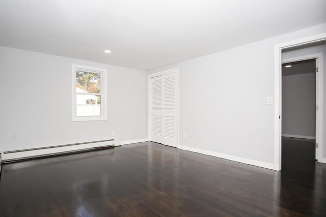 empty room featuring a baseboard heating unit and dark hardwood / wood-style flooring