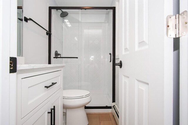 bathroom with a baseboard heating unit, hardwood / wood-style floors, walk in shower, toilet, and vanity