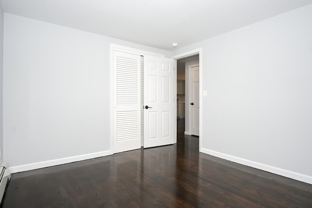 spare room featuring a baseboard heating unit and dark hardwood / wood-style flooring