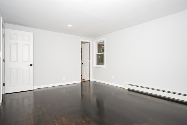 empty room featuring baseboard heating and dark wood-type flooring