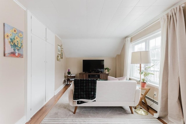 living room featuring a baseboard radiator, lofted ceiling, and light wood-type flooring