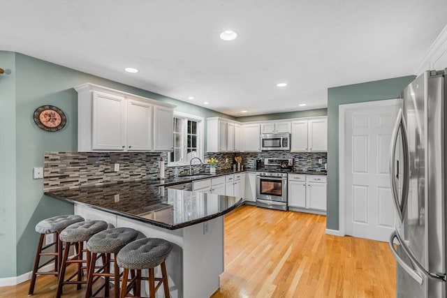 4 Kattail Rd, Hudson, MA 01749 - kitchen with appliances with stainless steel finishes, a peninsula, backsplash, light wood-type flooring, and dark stone countertops