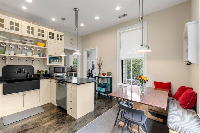 kitchen featuring a sink, a peninsula, dark countertops, stainless steel appliances, and visible vents