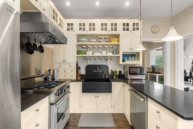 kitchen with a sink, a peninsula, under cabinet range hood, stainless steel appliances, and dark countertops