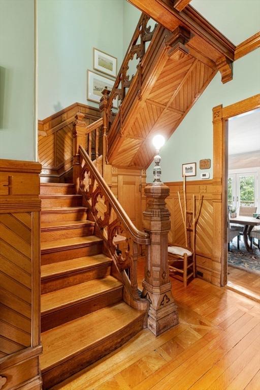 stairway with beamed ceiling, wooden walls, wainscoting, and hardwood / wood-style flooring