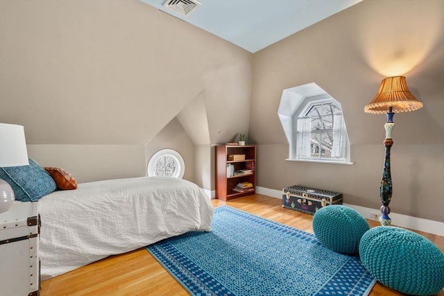 bedroom featuring baseboards, lofted ceiling, visible vents, and wood finished floors