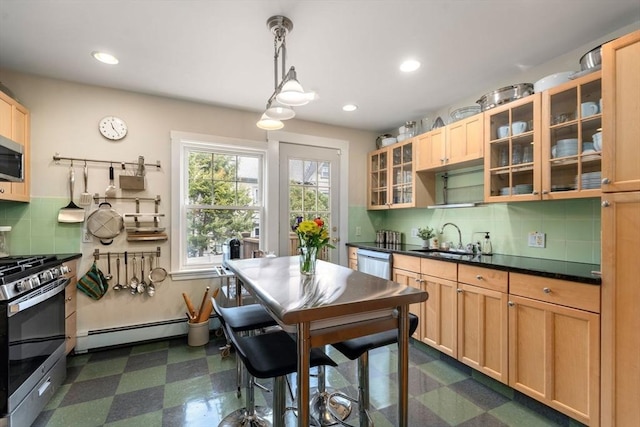 kitchen featuring a sink, appliances with stainless steel finishes, baseboard heating, dark countertops, and dark floors