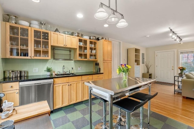 kitchen with stainless steel dishwasher, backsplash, a sink, dark countertops, and light brown cabinets