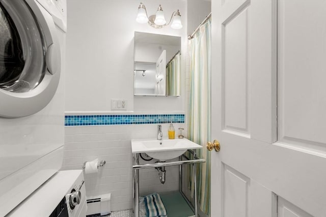 bathroom featuring stacked washer and dryer, a sink, wainscoting, a baseboard heating unit, and tile walls