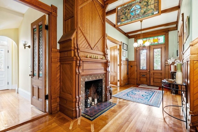 entrance foyer featuring crown molding, hardwood / wood-style floors, arched walkways, a high end fireplace, and wainscoting
