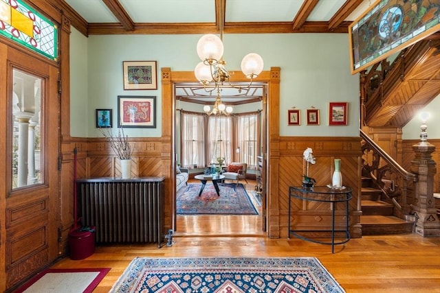 foyer entrance with a wainscoted wall, stairs, wood finished floors, radiator heating unit, and an inviting chandelier