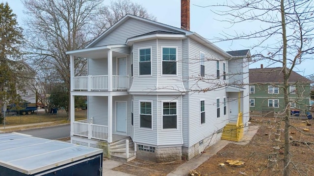 back of house with covered porch, a chimney, and a balcony