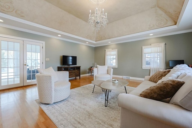 living room with french doors, an inviting chandelier, light wood-type flooring, ornamental molding, and a raised ceiling