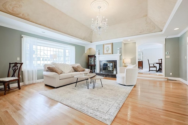 living room featuring crown molding, a chandelier, a raised ceiling, and light hardwood / wood-style floors