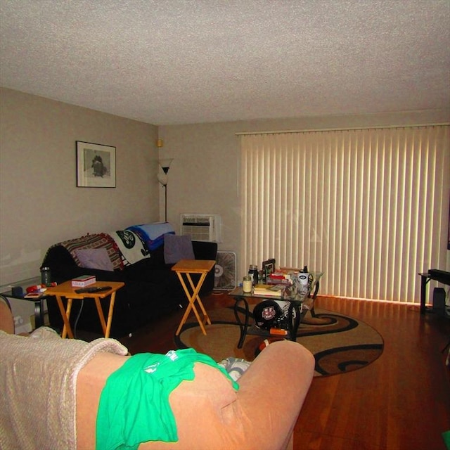 living room with a wall unit AC, hardwood / wood-style floors, and a textured ceiling