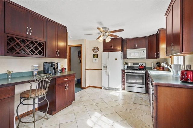 kitchen featuring ceiling fan, white appliances, a sink, dark brown cabinets, and dark countertops