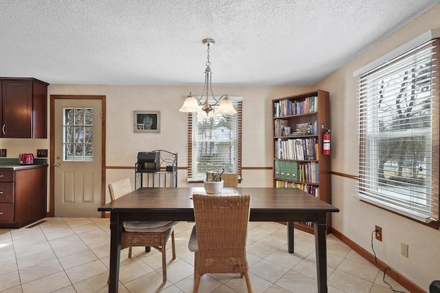 dining space featuring a chandelier, a textured ceiling, light tile patterned flooring, and baseboards