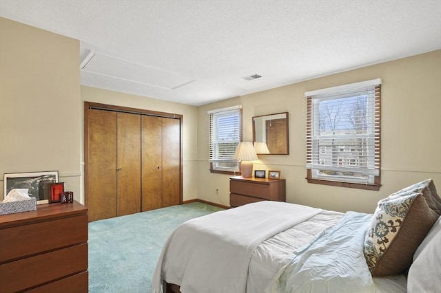 bedroom with a textured ceiling, carpet floors, visible vents, a closet, and attic access