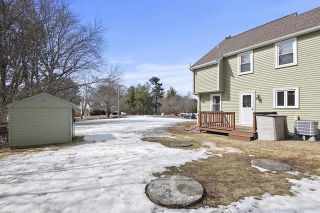 yard layered in snow featuring a deck, an outbuilding, cooling unit, a storage shed, and a garage